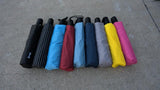 A photo of a lineup of many different colored umbrellas lying on a sidewalk. 