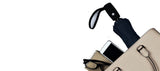 A zoomed in photo of a purse with a few items sticking out of to show the size of the umbrella relative to an iphone, glasses, notebook.