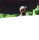 A photo of a man in a cap using a black golf umbrella with red spokes.